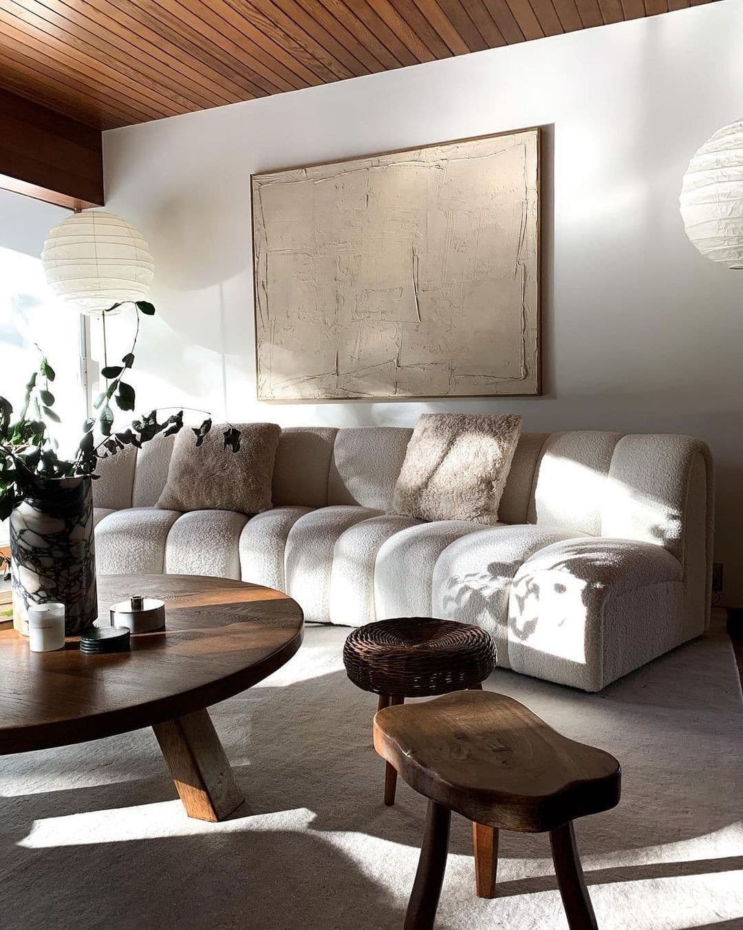 Sala de estar com luz natural, sofá modular de bouclé branco, mesa de centro de madeira e quadro texturizado